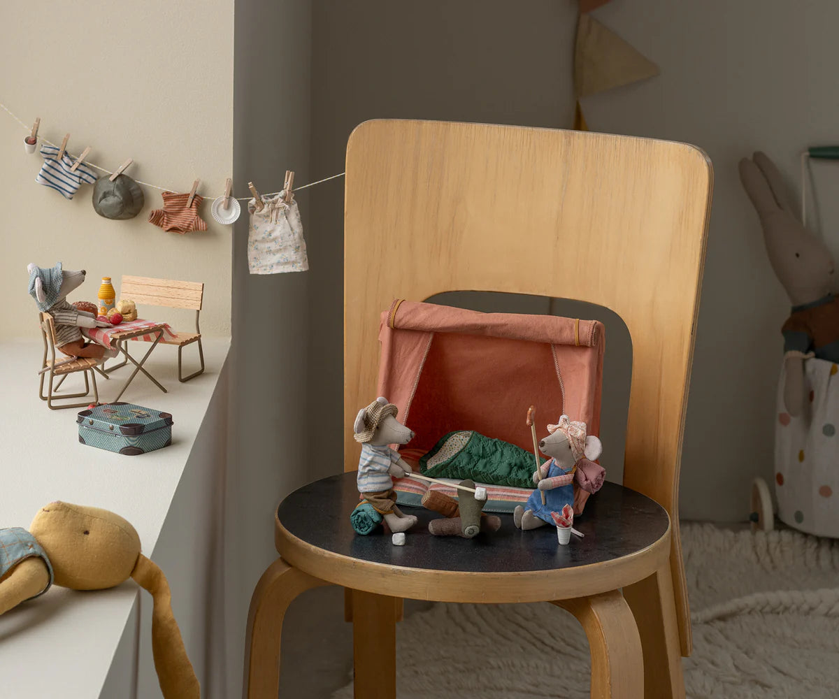 The Maileg Garden Set, Mouse features toy mice with camping gear by a small tent on a chair, another mouse at a picnic table, and doll clothes hanging on a string in this cozy outdoor scene.
