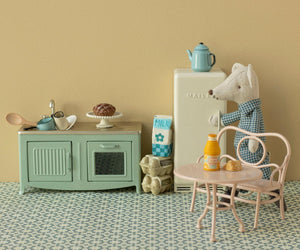 A Maileg Big Pale Pink Cafe Set - Mouse features a toy bear beside a miniature fridge and table, with orange juice, a croissant, and a cup, all styled in the charming Mouse Hole Farmhouse kitchen setting with delightful food accessories.
