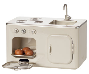 The Maileg Kitchen - Miniature is a charming metal kitchen set that includes a stovetop, sink, and an oven with an open door displaying a tray of three round pastries inside. Designed in perfect dollhouse scale, its metallic countertop and knobs add to the authentic detail.