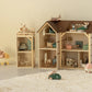 Maileg’s Mouse Hole Farmhouse Wallpaper sets a cozy scene, featuring wooden dollhouses with miniature furniture, toy mice, a car and stroller on a white floor beside a fluffy rug—perfectly enhanced by playful room stickers.