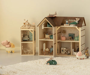 Maileg’s Mouse Hole Farmhouse Wallpaper sets a cozy scene, featuring wooden dollhouses with miniature furniture, toy mice, a car and stroller on a white floor beside a fluffy rug—perfectly enhanced by playful room stickers.