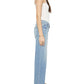 Woman in profile wears a white tank top, Mother Mid Rise Zip Rambler Skimp light blue denim wide straight leg jeans, and black flat sandals with white straps.