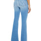 A person is seen from behind wearing Mother Denim High Waisted Weekender Fray jeans in a light blue, high-rise, stretch denim with a flared style, paired with high heels, set against a white background.