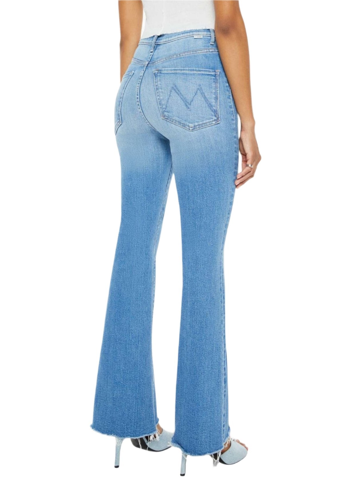 A person is seen from behind wearing Mother Denim High Waisted Weekender Fray jeans in a light blue, high-rise, stretch denim with a flared style, paired with high heels, set against a white background.