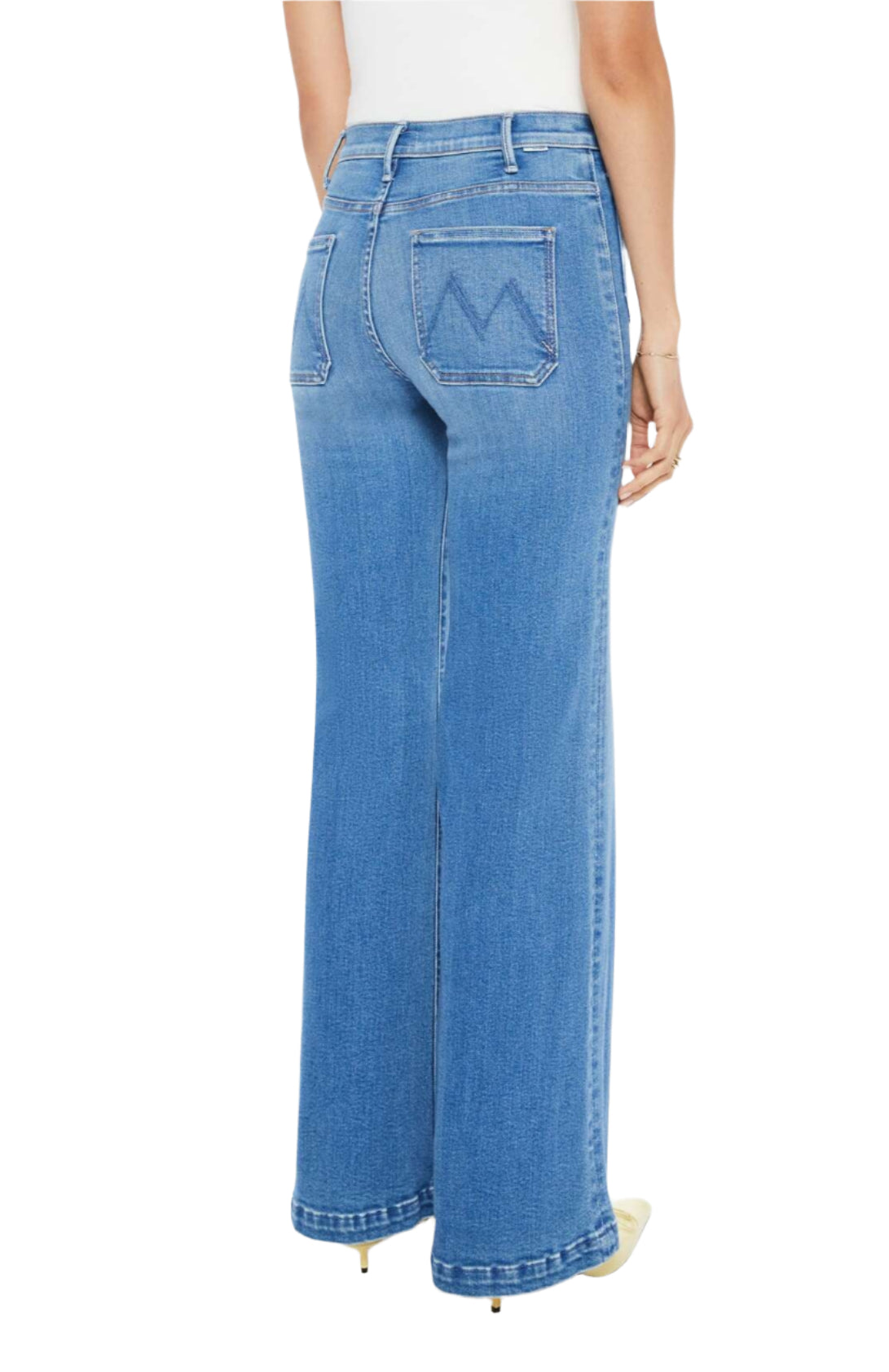 A person is wearing Mother Denim Hustler Roller Patch Pocket Sneak jeans, featuring high-waisted, wide-leg blue stretch denim and a distinctive "W" design on the back pockets, seen from behind.