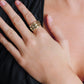 A person wears the Anabel Aram Farrier Triple Connected Ring—a large, gold, hammered ring—on their middle finger, resting their hand on their chest while dressed in black.