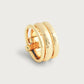 The Anabel Aram Farrier Triple Connected Ring features a gold-tone wide band with a hammered texture and overlapping, belted design, shown against a plain light background, highlighting its unique style.
