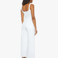 A woman stands facing away, wearing Mother’s The Ditcher Roller Zip Ankle jeans with a white tank top and brown sandals against a plain white background.