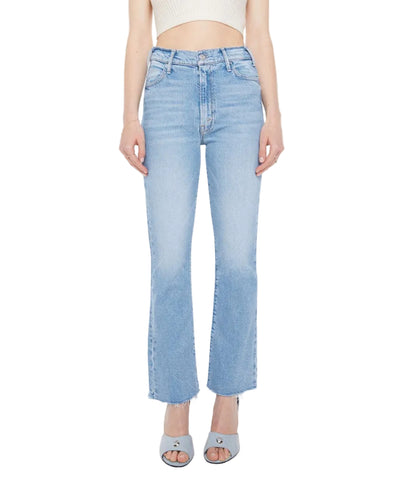 A person wearing Mother The Hustler Ankle Fray high-waist flare jeans in light blue, a white sleeveless crop top, and light blue open-toe heels stands against a white background.