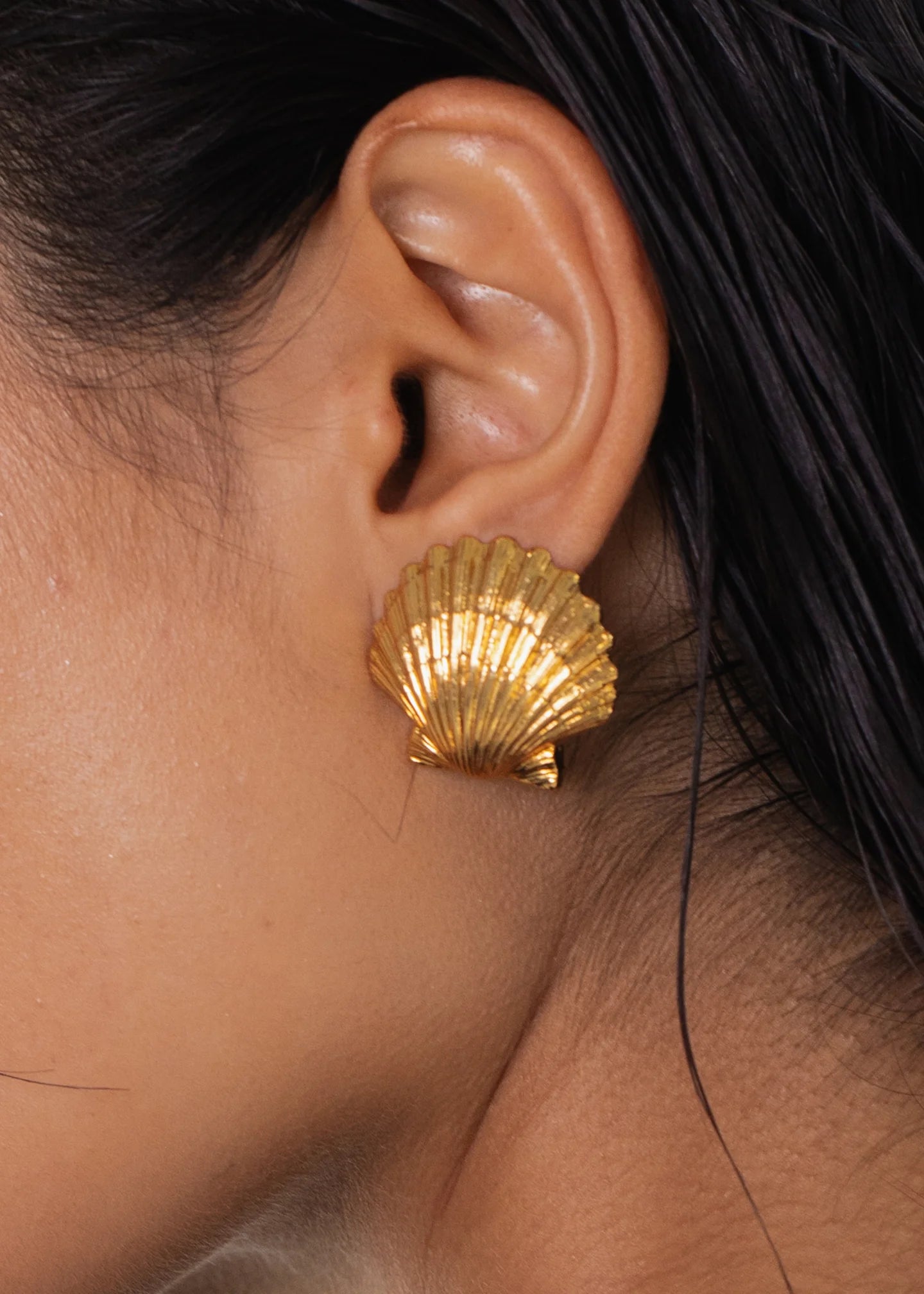 Close-up of a person's ear wearing Mar Earrings by Jennifer Behr, crafted in the shape of a golden scallop shell.