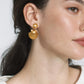 Close-up of a woman wearing Jennifer Behr's Caspian Earrings, crafted in 18-karat gold-plated metal with a seashell silhouette, her hair tucked behind her ear and a neutral expression.