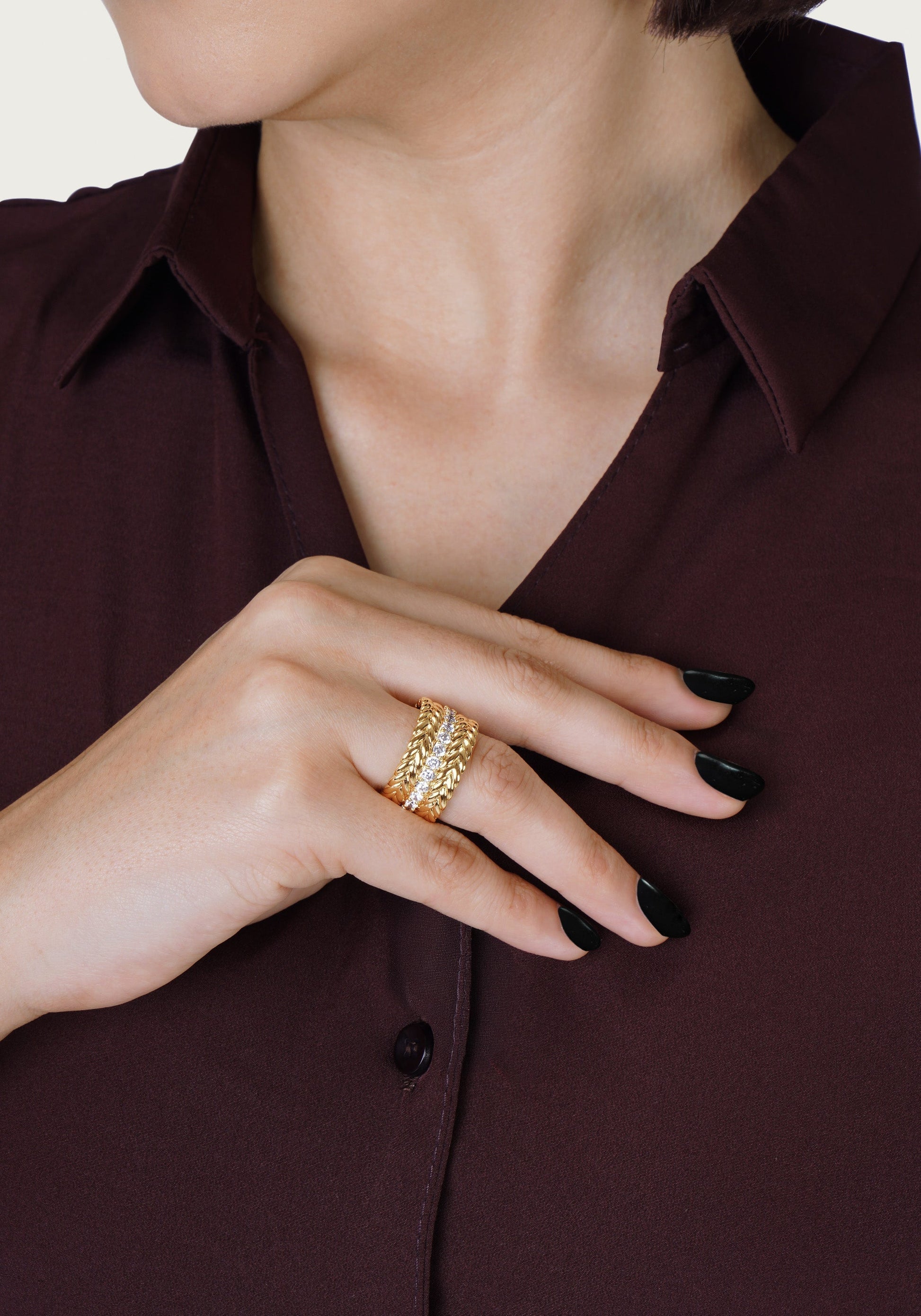 A person in a burgundy shirt shows their black-painted nails and three stacked gold rings, including the Anabel Aram Cheval Chain Stack Ring.