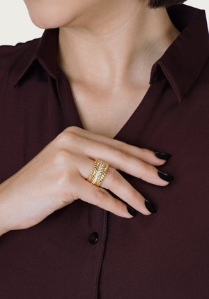 A person in a burgundy shirt shows their black-painted nails and three stacked gold rings, including the Anabel Aram Cheval Chain Stack Ring.