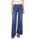 Person wears The Undercover high-rise, wide leg jeans from Mother, crafted from recycled stretch denim, paired with a white sleeveless top and standing with arms relaxed at their sides.