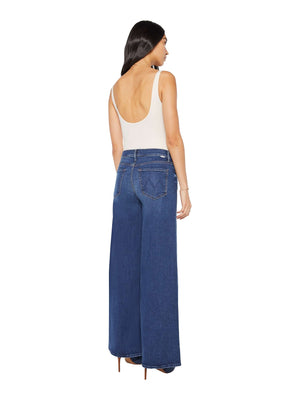 A woman modeling The Undercover by Mother— a sleeveless, low-back beige top paired with high rise wide leg recycled stretch denim jeans—stands facing away against a white background.