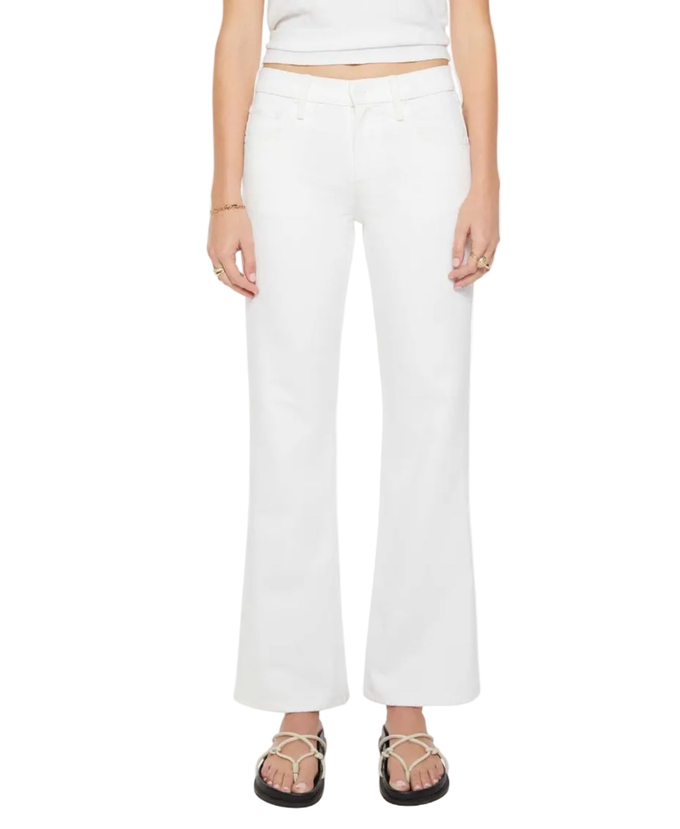 A person wearing Mother’s The Bookie Skimp high-waisted white denim jeans stands facing forward, paired with a white tank top, black sandals, and simple jewelry. Only the lower torso and legs are visible.