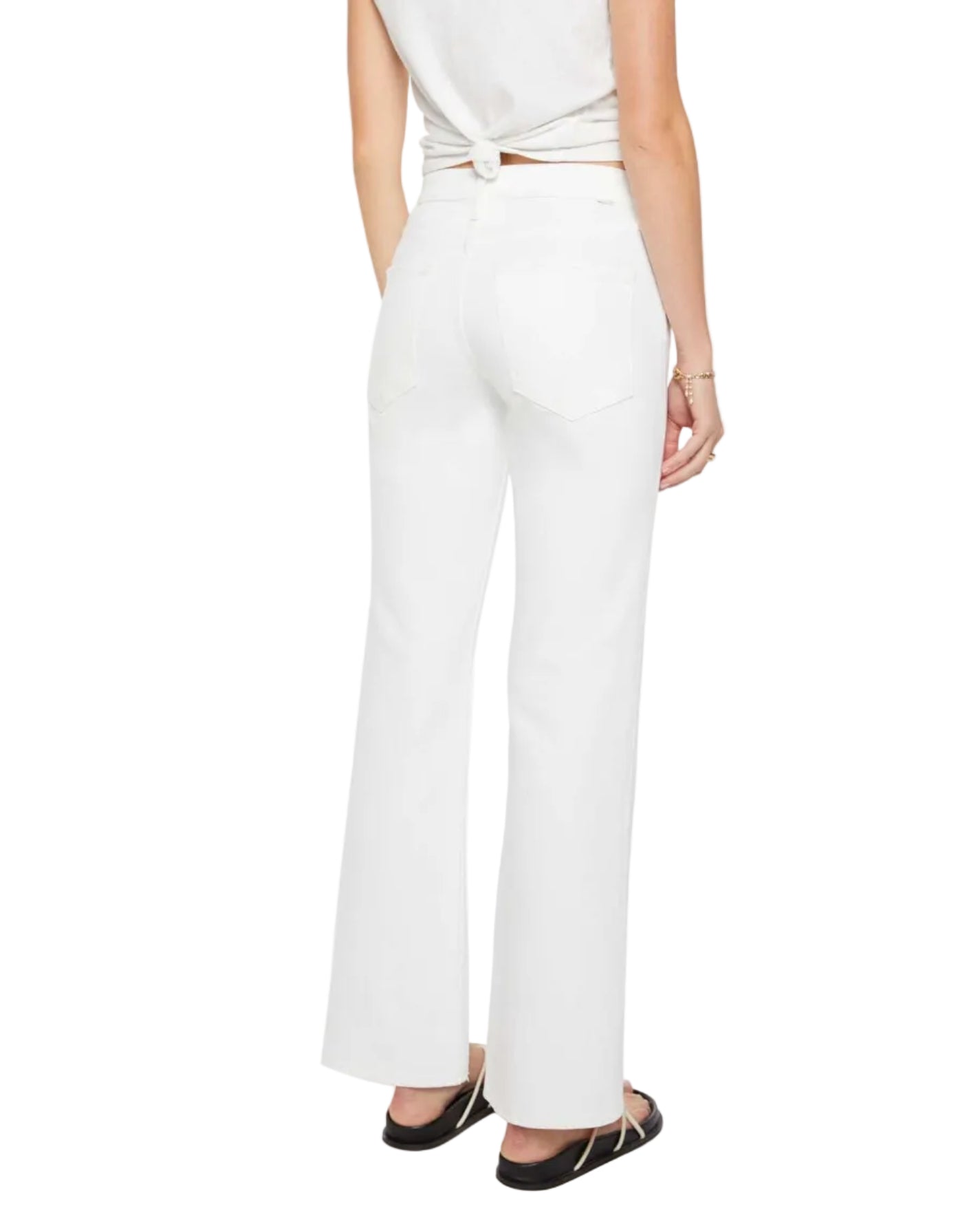 A person is shown from the back against a plain background wearing Mother’s The Bookie Skimp high-waisted white denim flared jeans, paired with a white sleeveless top tied at the back and black flat sandals.