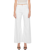 A person is wearing The Lemon Twist Skimp high-rise, wide leg pants by Mother in a rigid cotton blend, paired with a sleeveless beige top and black open-toe heels, standing against a plain white background.