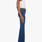 A woman stands in profile against a plain white background, wearing Mother’s The Patch Pocket Doozy high-rise flare jeans in dark blue stretch denim, paired with a sleeveless white top and sandals.