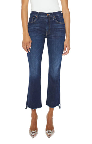 Model wears The Insider Crop Step Fray jeans by Mother, featuring dark blue stretch denim, a frayed step-hem, and cropped flare style, paired with clear embellished pointed-toe heels against a white background.