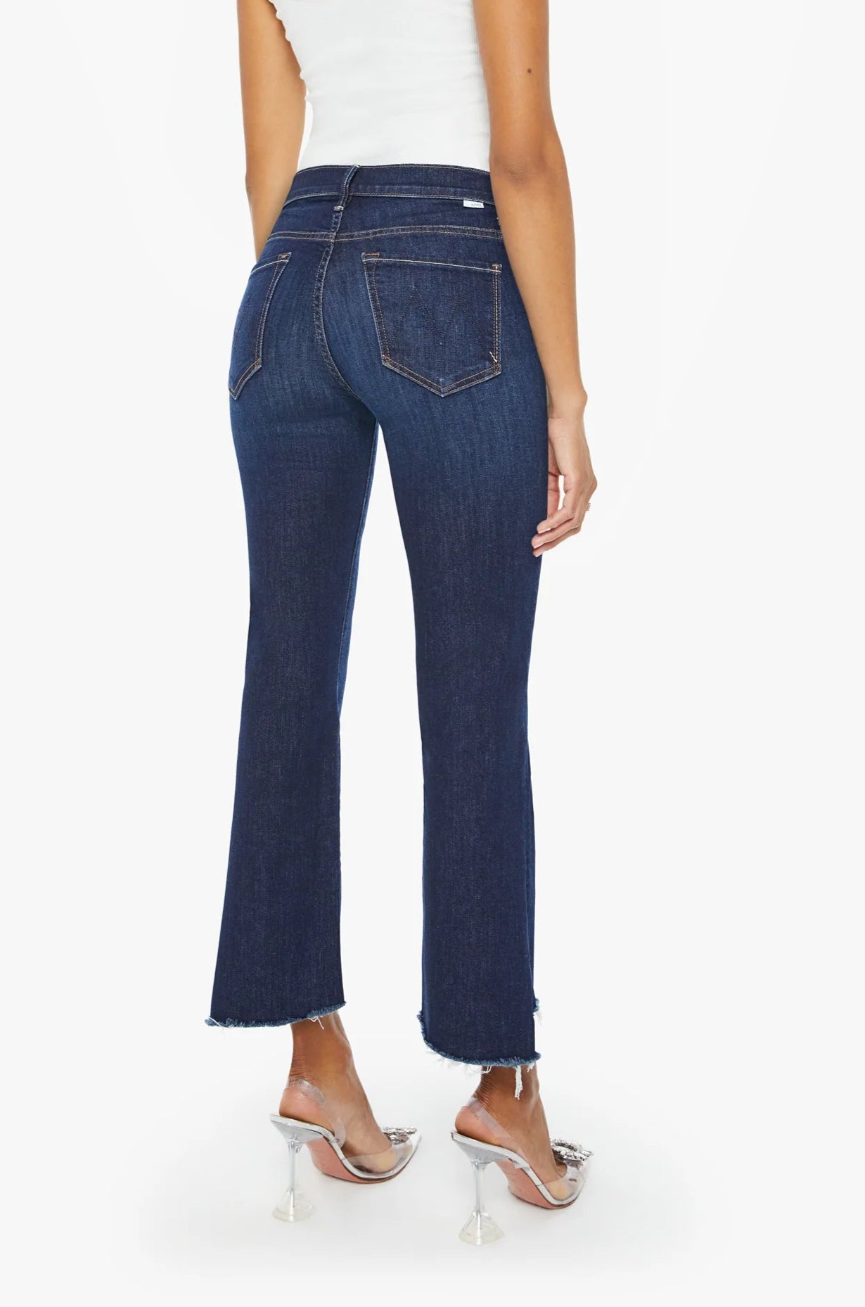 Woman shown from the back wearing Mother's The Insider Crop Step Fray dark blue high-waisted bootcut jeans with a frayed step-hem, a white sleeveless top, and clear high-heeled sandals.