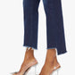 Someone wearing Mother’s The Insider Crop Step Fray high-waisted bootcut blue jeans with a frayed step-hem and clear, embellished pointed-toe heels, standing against a white background.