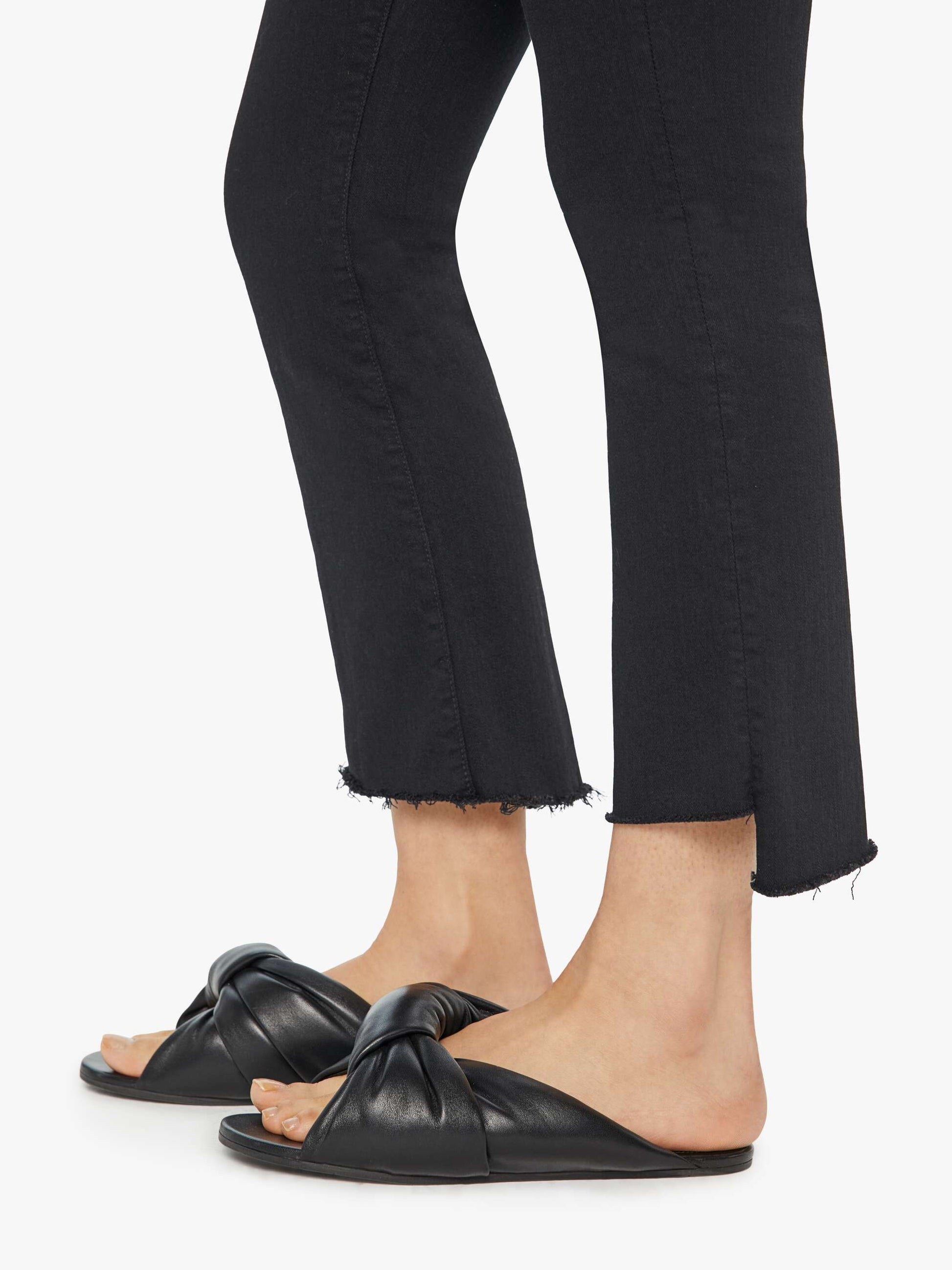A person wearing black slide sandals and Mother’s The Insider Crop Step Fray jeans, photographed from the knees down against a white background.
