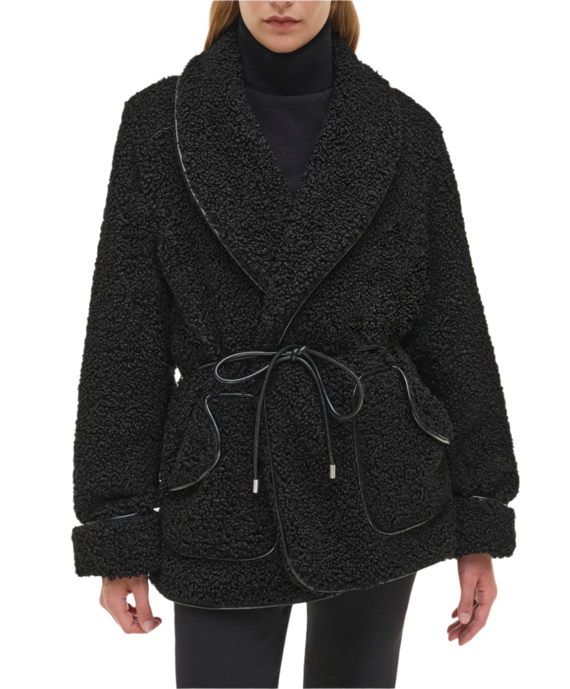 A person wearing the Simkhai Kimia Tie Waist Jacket—a black textured coat with a foldover collar, large lapels, front pockets, cuffed sleeves—paired with a black turtleneck and pants.