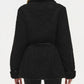 A person seen from the back wears the Simkhai Kimia Tie Waist Jacket, a black textured coat featuring a tie front closure, wide foldover collar, and cuffed sleeves.