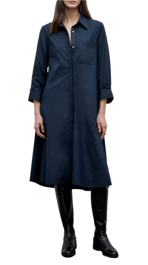 A woman wears the TWP Hankerchief Midi Jenny's Gown, a navy blue long-sleeve button-down dress with a chest pocket, styled with black knee-high boots.