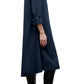 A person stands in profile against a white background wearing the TWP Hankerchief Midi Jenny's Gown, a navy blue long-sleeve cotton shirtdress, paired with black knee-high boots.