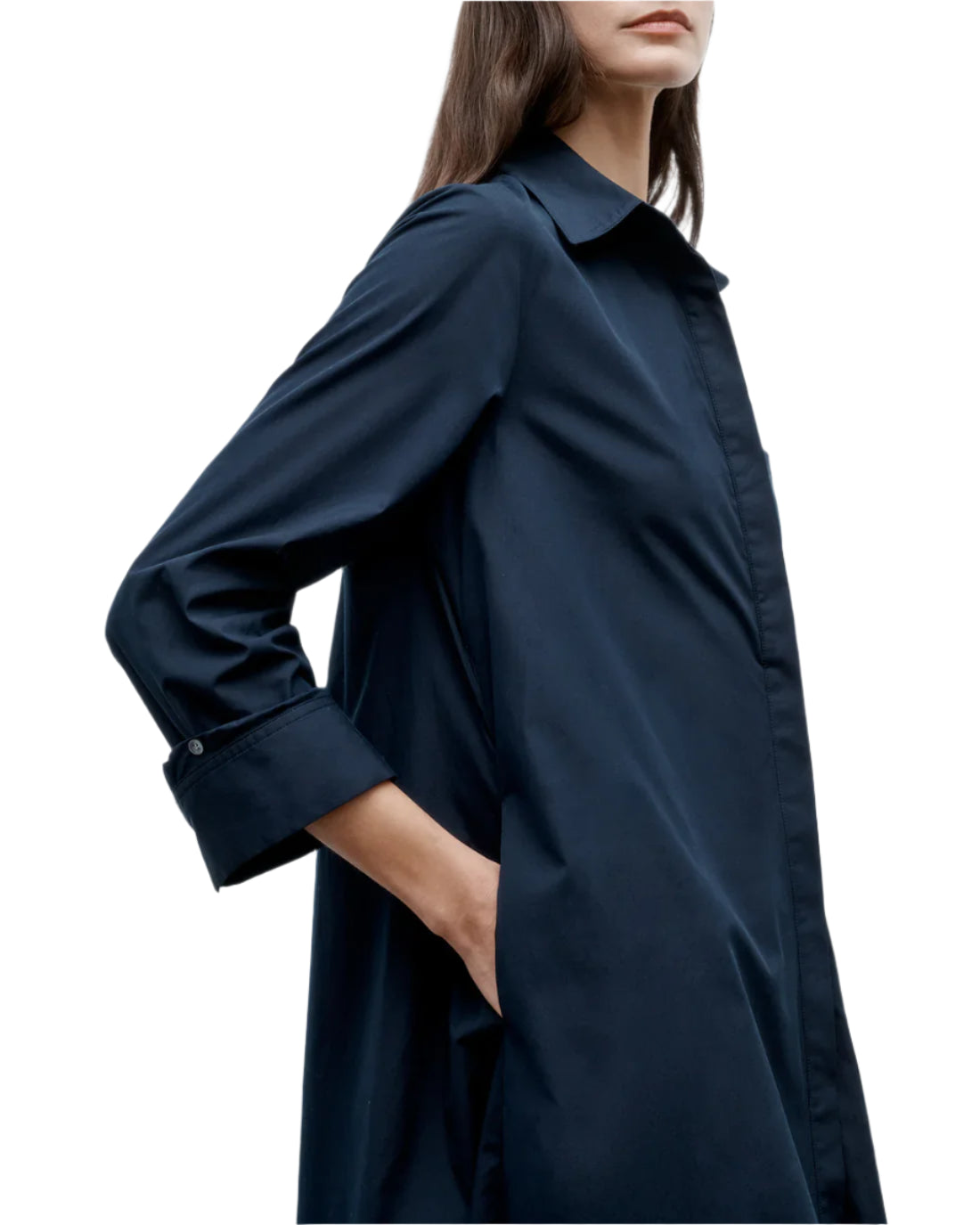 A woman wearing the TWP Hankerchief Midi Jenny's Gown, a long-sleeve dark blue cotton collared shirt dress with her hand in the pocket, shown from shoulders to mid-thigh.