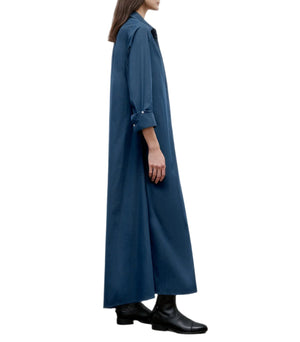 A person in profile models the Jenny's Cotton Gown by TWP, an oversized maxi shirt dress made from Italian cotton shirting with rolled sleeves, styled with black boots against a white background.