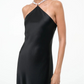 A woman wears the Staud Cadence Dress, a black satin slip with beaded pearl straps, shown against a plain white background.