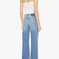A woman stands with her back to the camera against a plain white background, wearing a white sleeveless top paired with Mother’s The Bookie Twist Skimp high-waisted, light blue bootcut jeans crafted from superior denim, and light-colored heels.