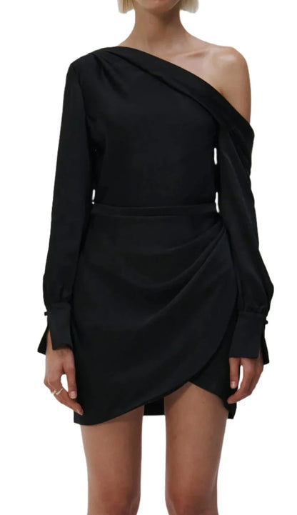 A person wearing a black Simkhai Cameron One Shoulder Mini Dress, crafted from high sheen satin, featuring a one-shoulder design and a wrap-style skirt.