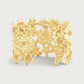 The Anabel Aram Wildflowers Gold Wide Cuff features an intricate raised floral design and a radiant 18k gold plated finish, making it a standout statement piece.