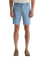 A person wearing light blue AG Jeans Wanderer Shorts, a white shirt, and brown loafers showcases a tailored look against a plain white background.