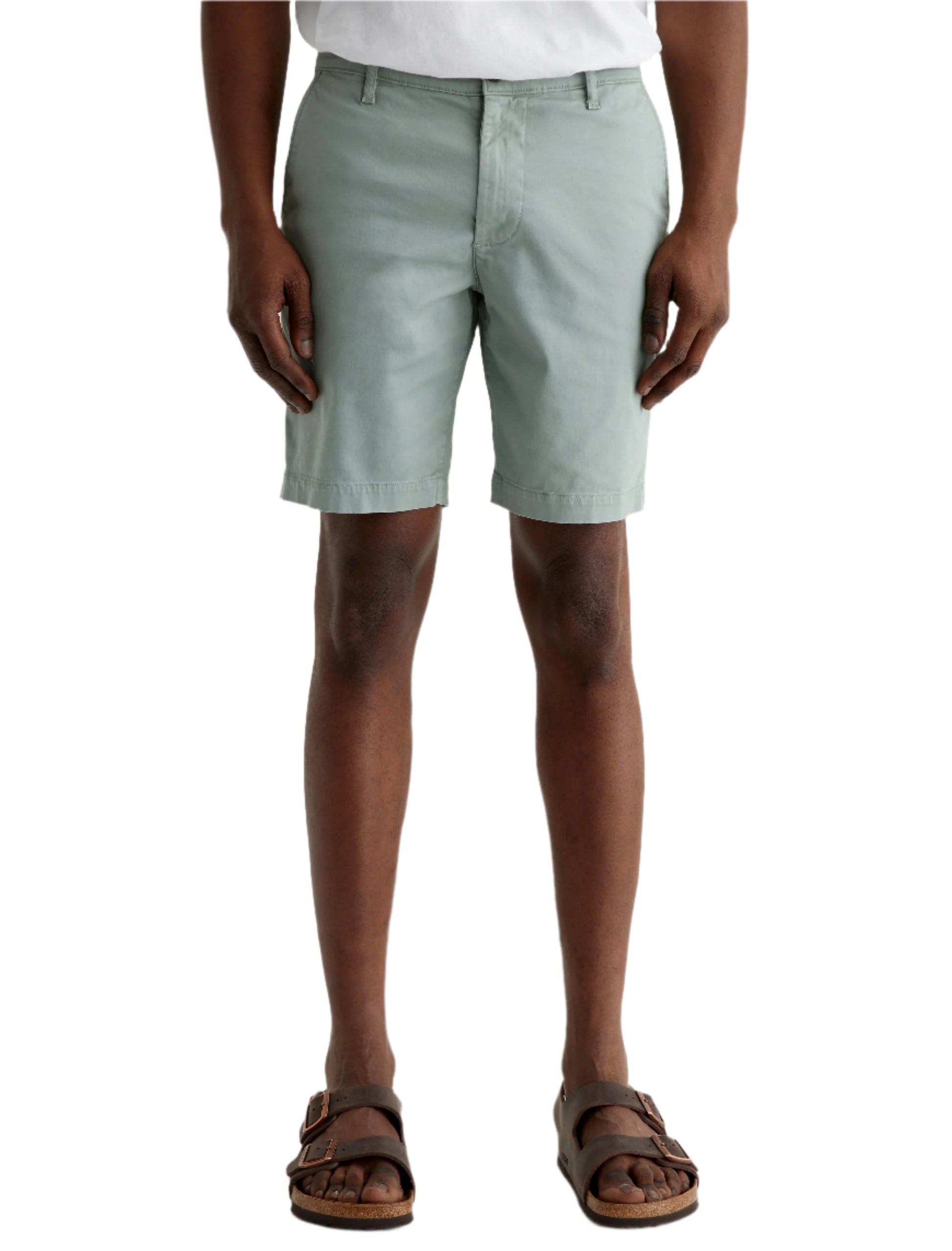 A person wears light green AG Jeans Wanderer Shorts, a white shirt, and brown sandals, standing against a plain background for a tailored look.