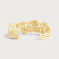 The Anabel Aram Wildflowers Bangle is an 18k gold open cuff bracelet featuring an intricate floral and leaf design, adding elegance to any look.