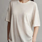 Person wearing a TWP Big Boy Skye Cashmere Tee, an oversized white t-shirt with a chest pocket, and hands in the pockets of brown pants, standing in front of a neutral background.