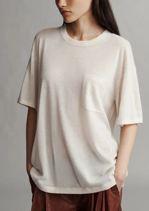 Person wearing a TWP Big Boy Skye Cashmere Tee, an oversized white t-shirt with a chest pocket, and hands in the pockets of brown pants, standing in front of a neutral background.