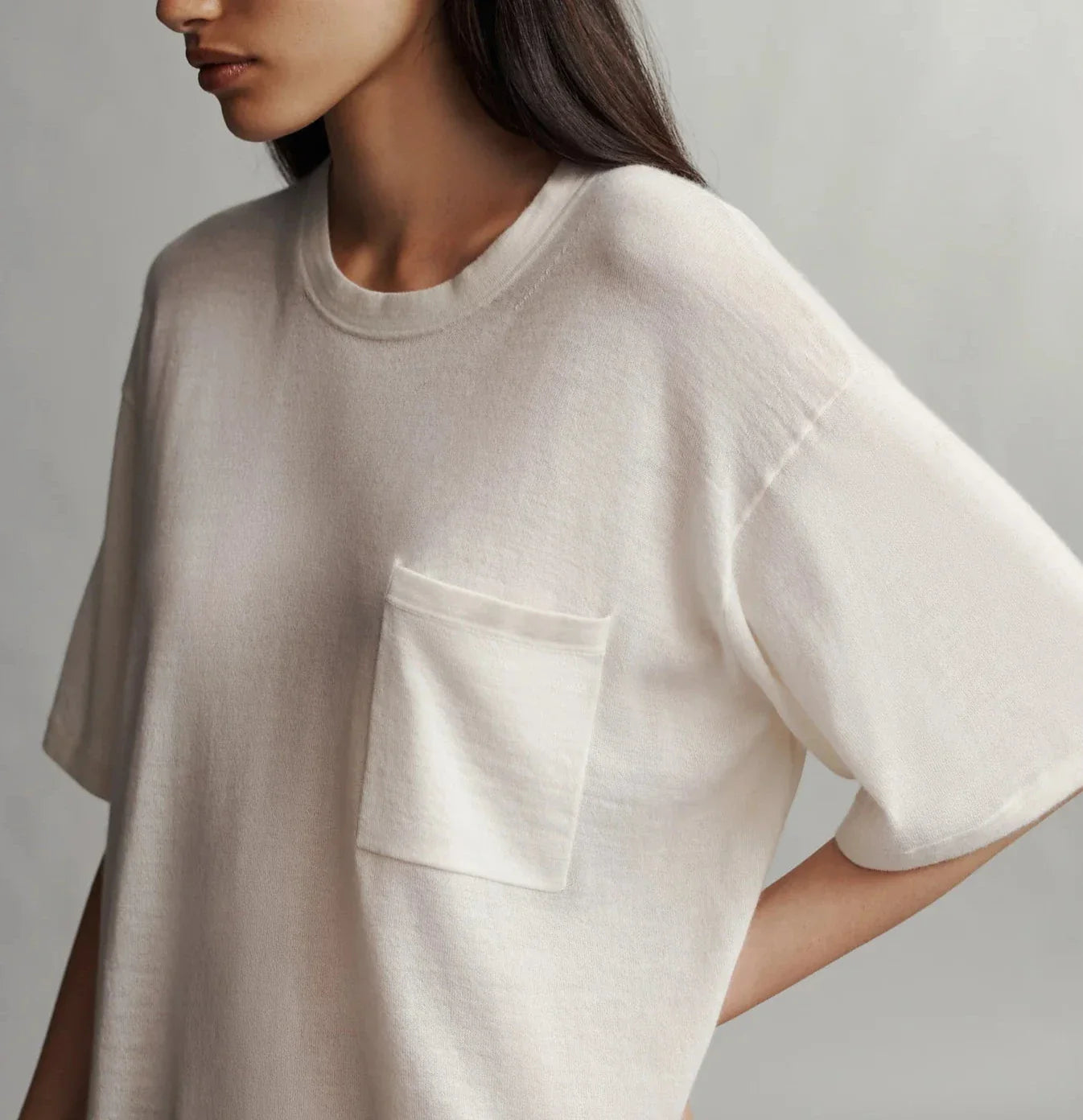 A person wearing a loose-fitting, short-sleeved TWP Big Boy Skye Cashmere Tee with a front pocket. Their head is only partially visible, and the background is neutral.