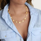A woman wears the Anabel Aram Wildflowers Station Necklace, a nature-inspired gold piece, over a light blue shirt against a plain background.