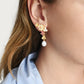 Close-up of a woman wearing Anabel Aram Wildflowers Pearl Drop Earrings—handcrafted 18k gold earrings with pink stones and a dangling pearl—shown in profile with a light blue shirt collar.