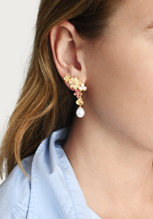 Close-up of a woman wearing Anabel Aram Wildflowers Pearl Drop Earrings—handcrafted 18k gold earrings with pink stones and a dangling pearl—shown in profile with a light blue shirt collar.