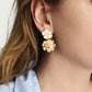 Close-up of a woman's ear wearing Anabel Aram’s Wildflowers Mixed Drop Earrings—double flower-shaped gold drops featuring a small white stud and a larger gold bloom.