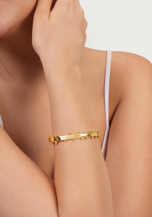 A person wearing an Anabel Aram Milos Gold Hinged Bangle on their wrist, paired with a white sleeveless top.