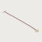 The Cheval Leather Wrap Bracelet by Anabel Aram features a slim red leather cord with gold-tone T-bar and D-shaped clasp, inspired by equestrian style—ideal for daily wear. Shown against a white background.