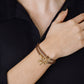 A person wearing a black textured shirt and the Anabel Aram Cheval Leather Wrap Bracelet with gold accents on their wrist, one hand resting on their collarbone.